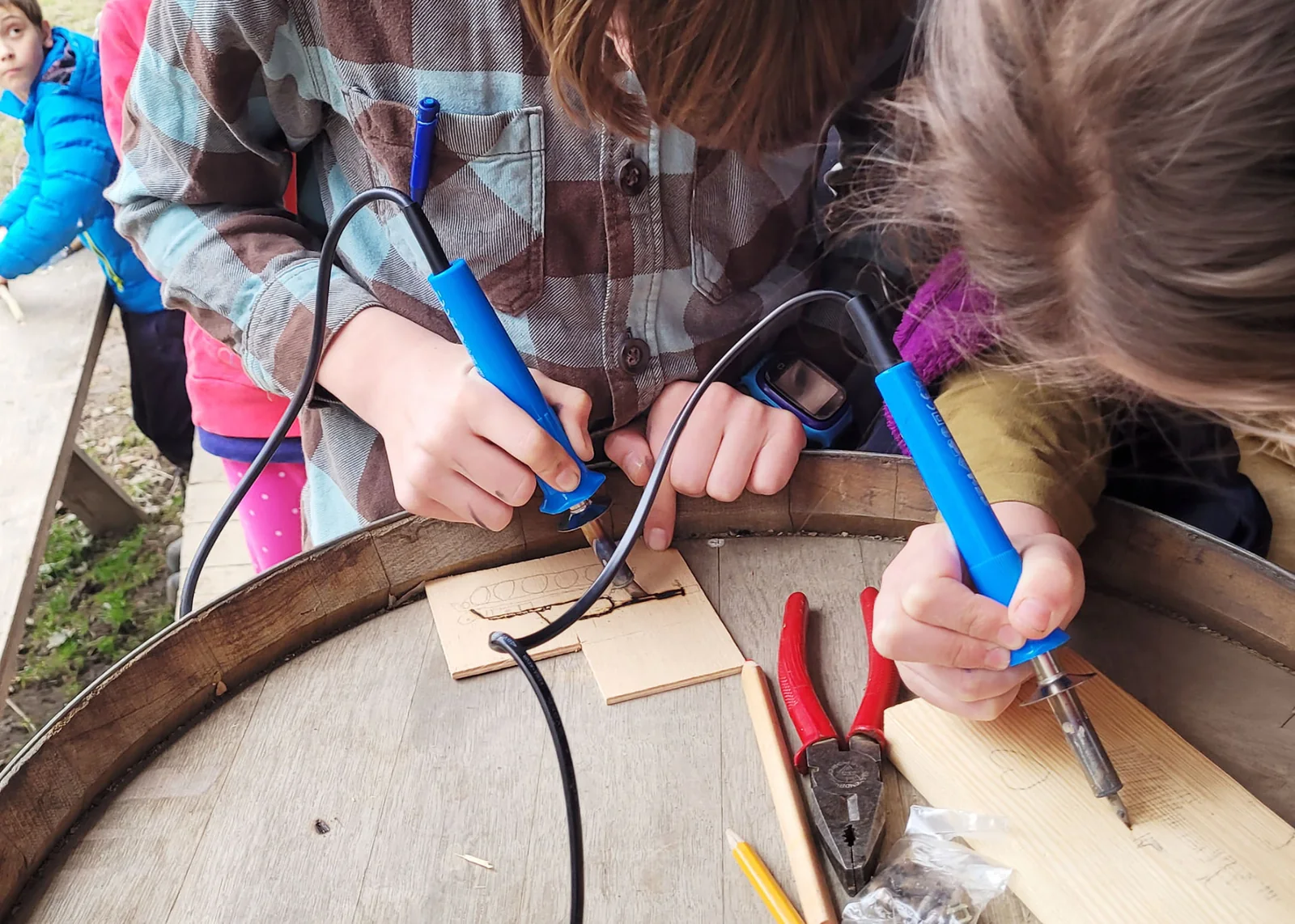 Děti vypalují vzory do dřeva pyrografem u altánu