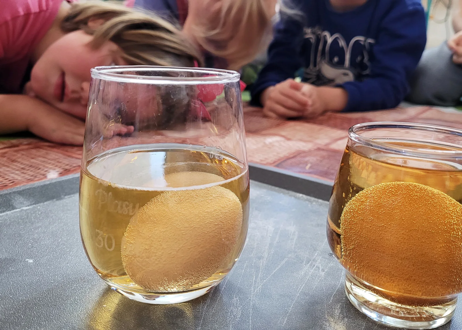 Pokus s vejcem ve skleničce s tekutinou, děti v pozadí